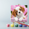 An easel with paints and a puppy in a basket paint by number canvas on it