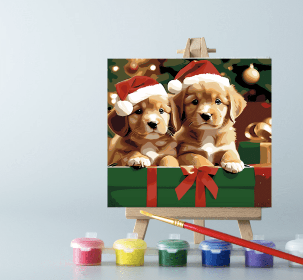 Paint by number Christmas puppies painting displayed on an easel, accompanied by paint pots and a brush, perfect for holiday crafting and creativity.