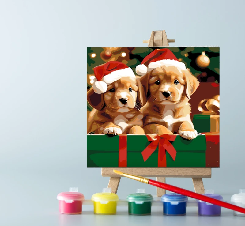 Paint by number Christmas puppies painting displayed on an easel, accompanied by paint pots and a brush, perfect for holiday crafting and creativity.
